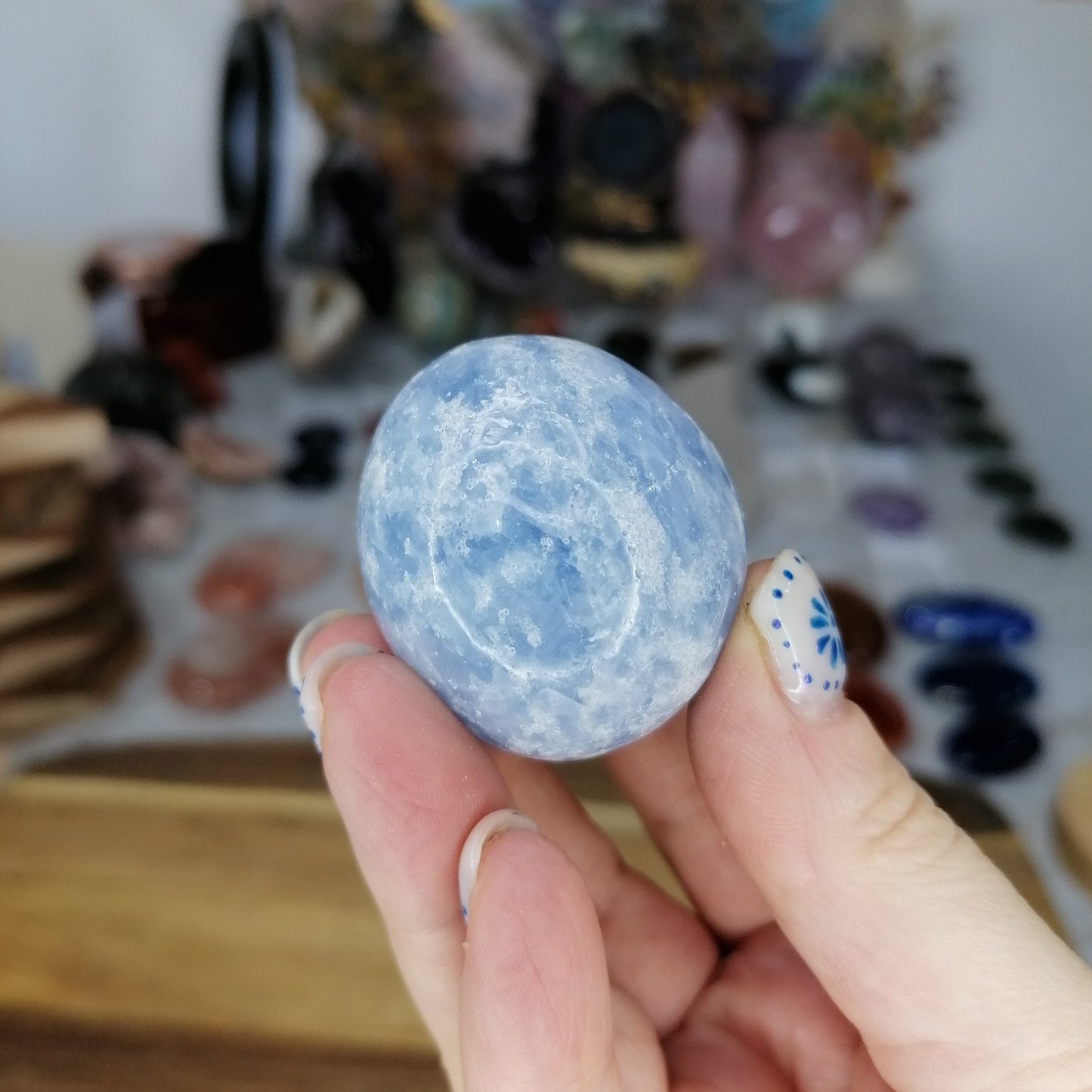 Hand holding a blue calcite crystal ball with a blurred background of various items.