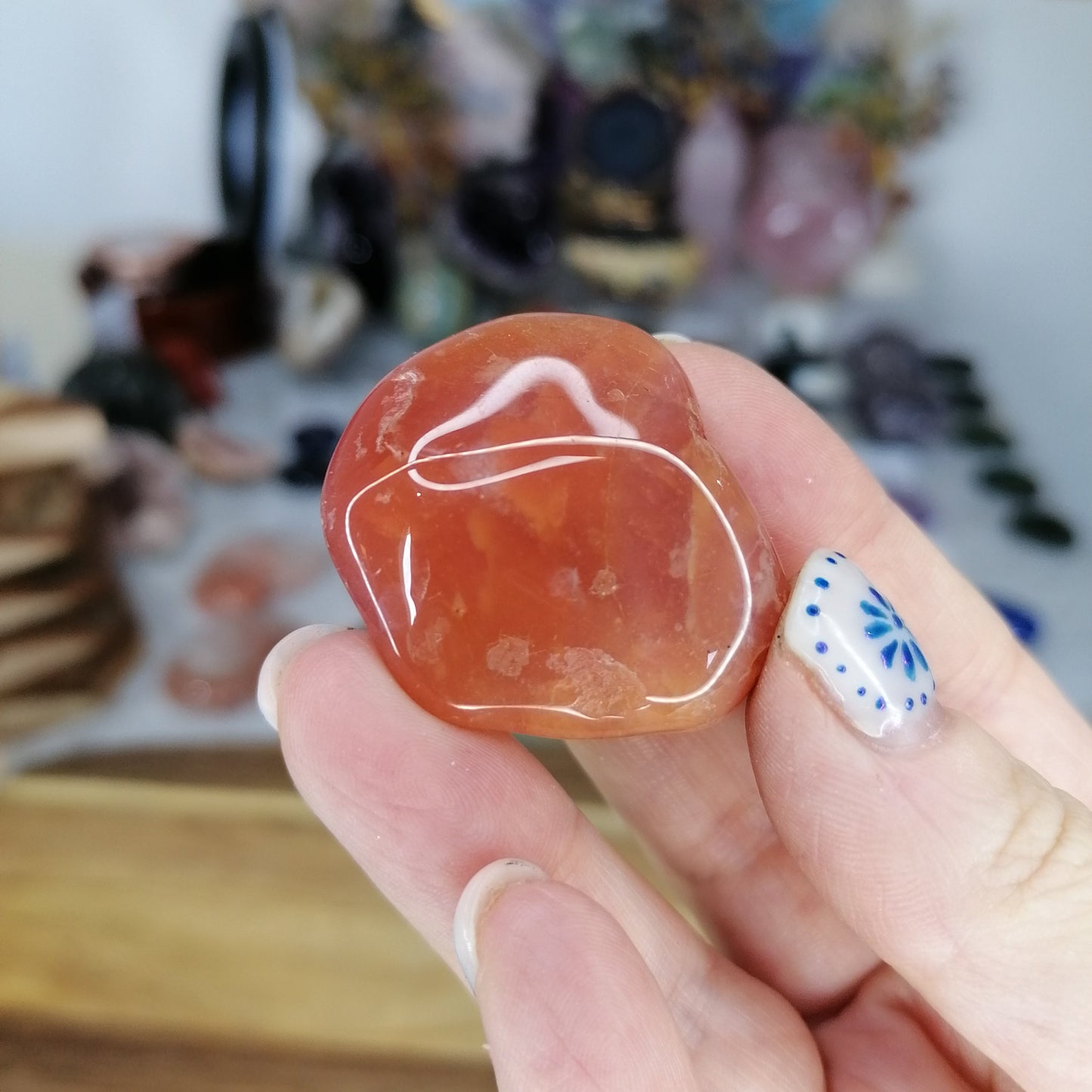 Hand holding a red-orange carnelian crystal with white markings against a blurred background