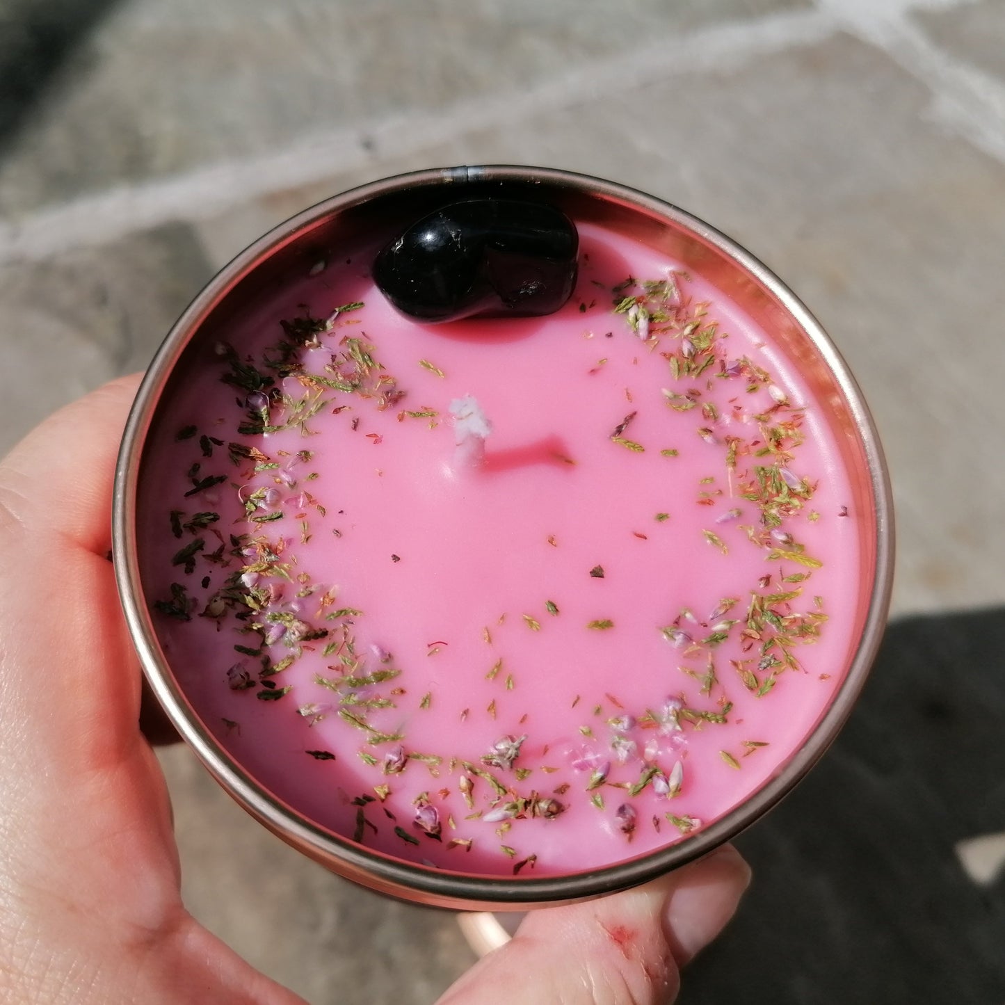 a pink candle in a rose gold tin with a black onyx crystal and scottish heather