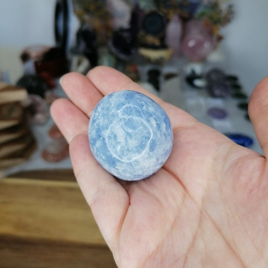 Hand holding a blue and white marbled stone known as Blue Calcite