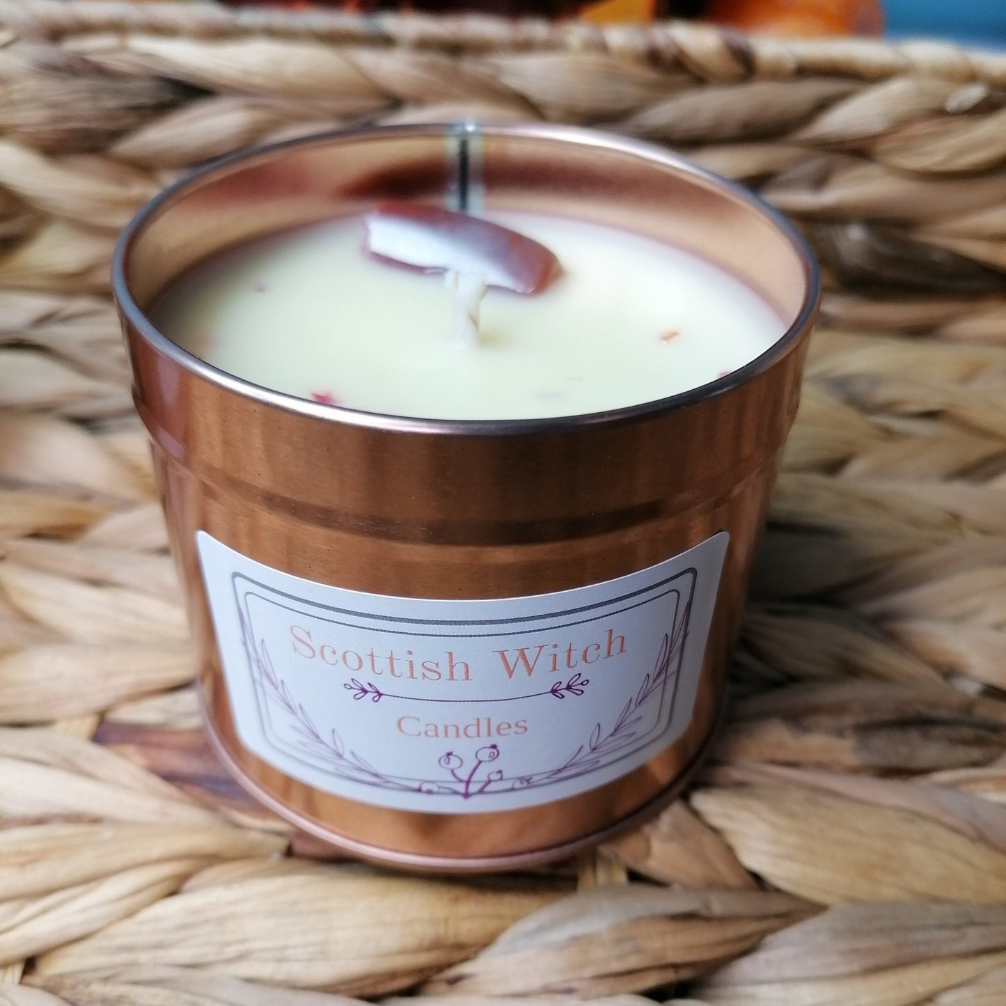 A white candle in a rose gold tin that has a fresh linen scent and is decorated with colourful jasper crystal and glitter