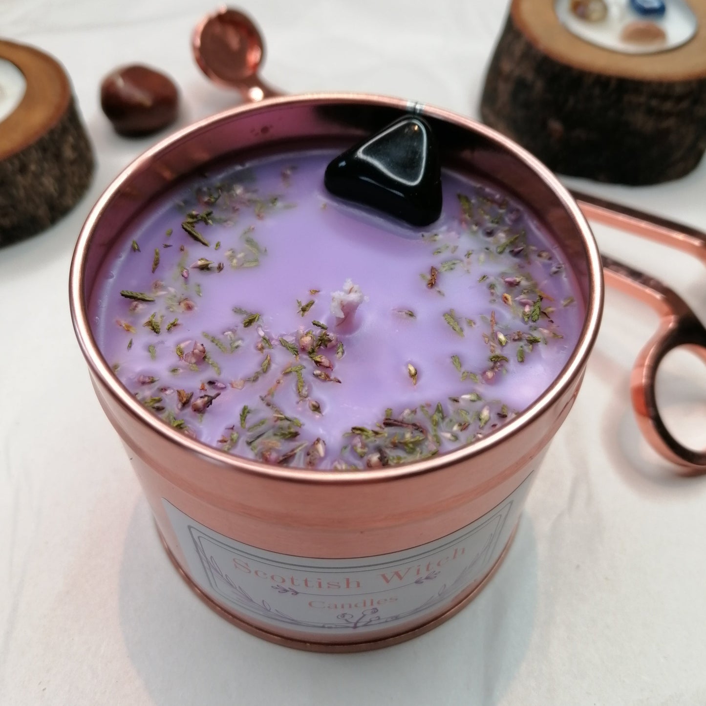 purple candle in a rose gold tin decorated with a black onyx crystal and scottish heather