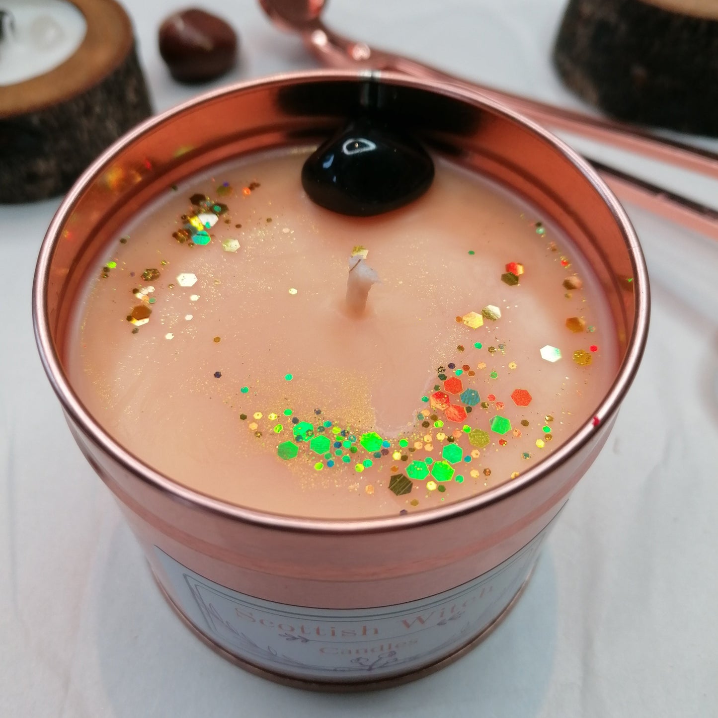 orange candle in a rose gold tin decorated with a black onyx crystal and glitter