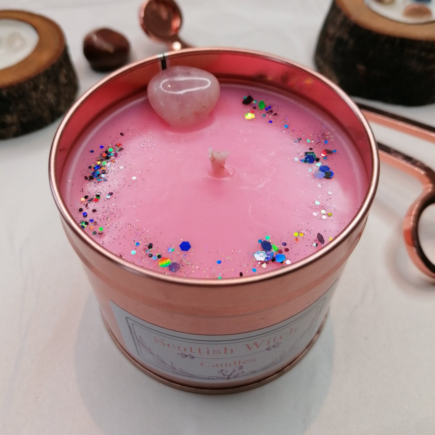 pink candle in a rose gold tin decorated with a rose quartz crystal and glitter