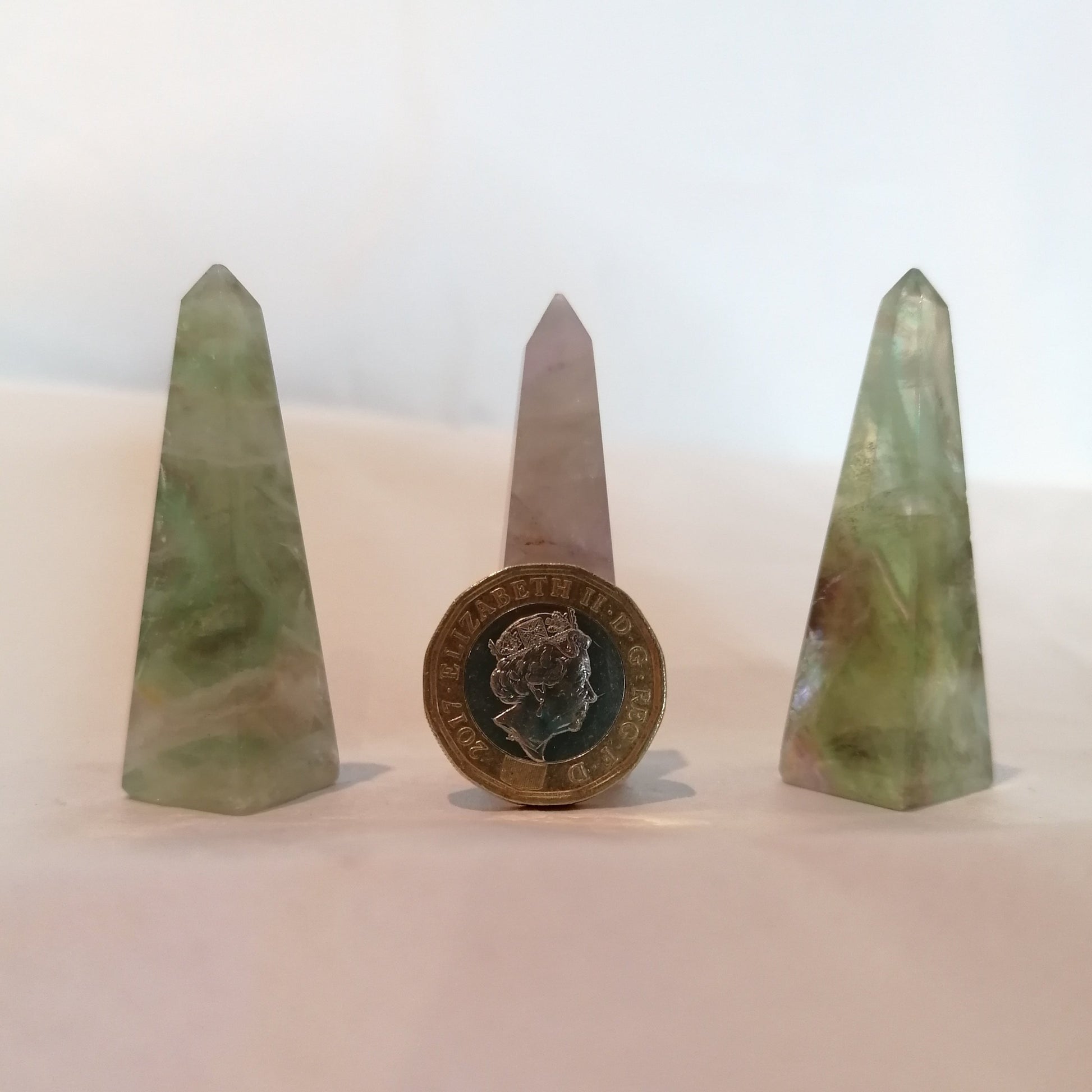 three purple and green fluorite crystal obelisks with a £1 coin to show size