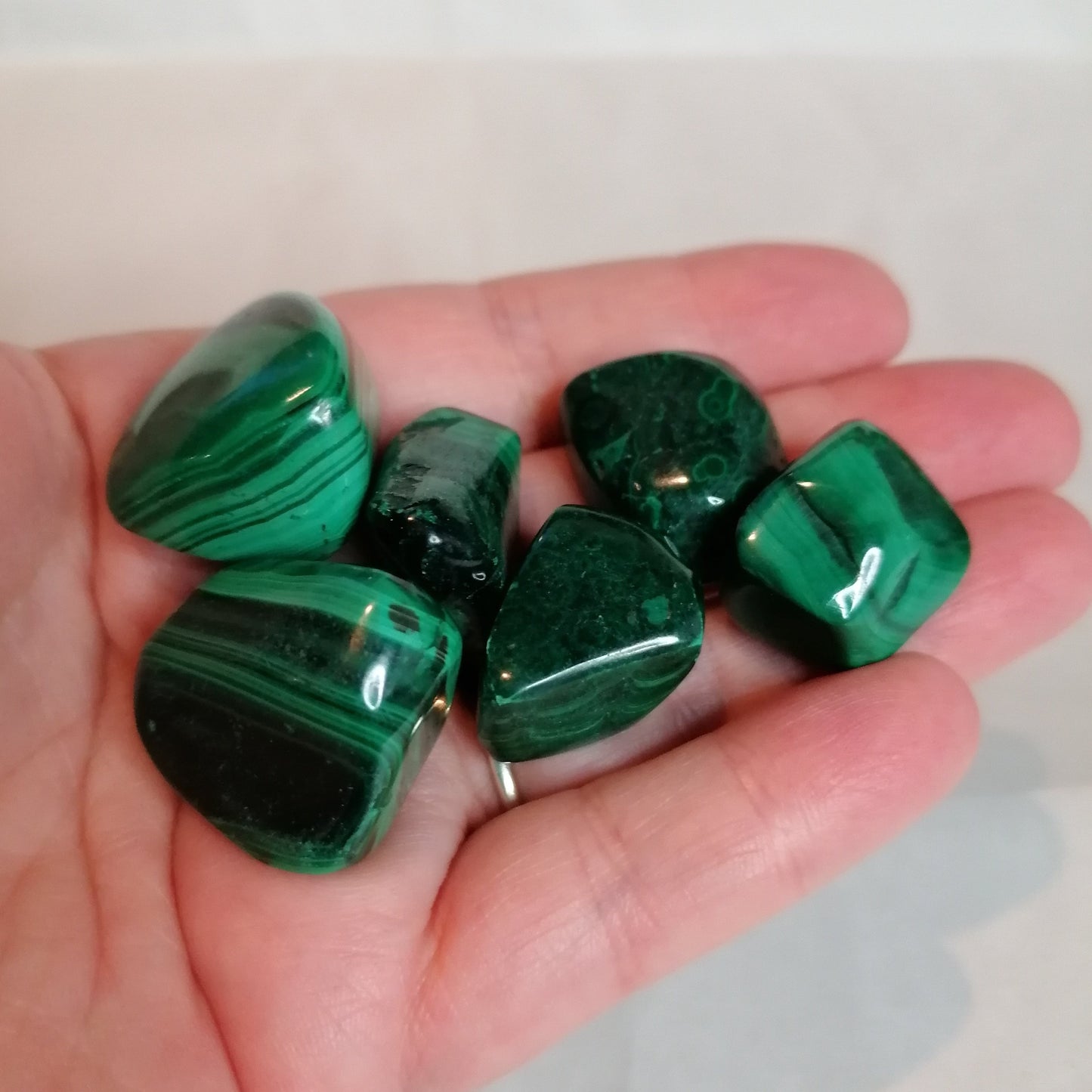 6 green malachite crystal tumbles held in a hand to show size