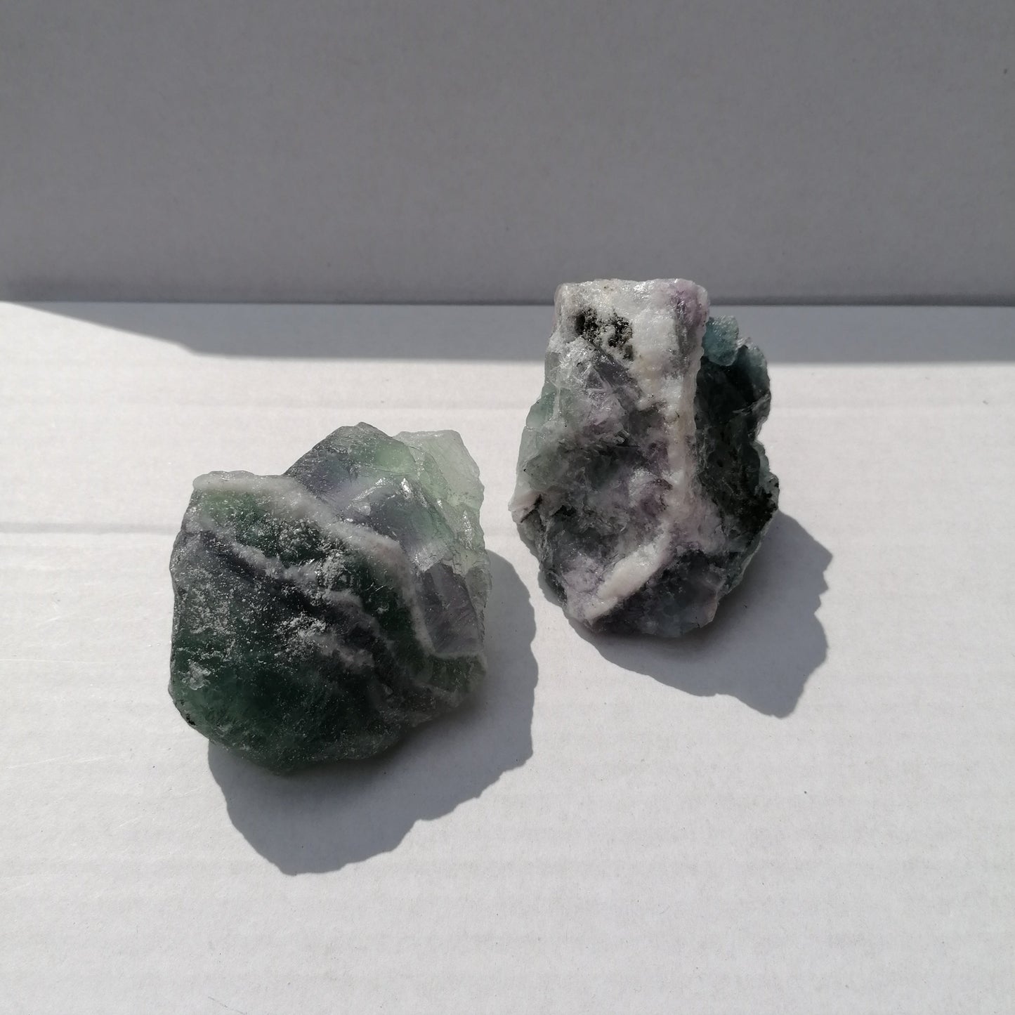 two pieces of green, purple and white fluorite raw chunks