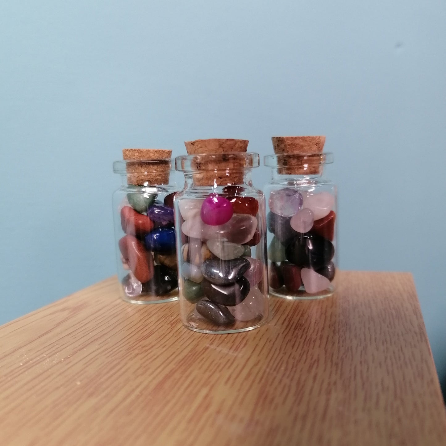 three small glass bottles filled with multi colour crystal chips on a shelf