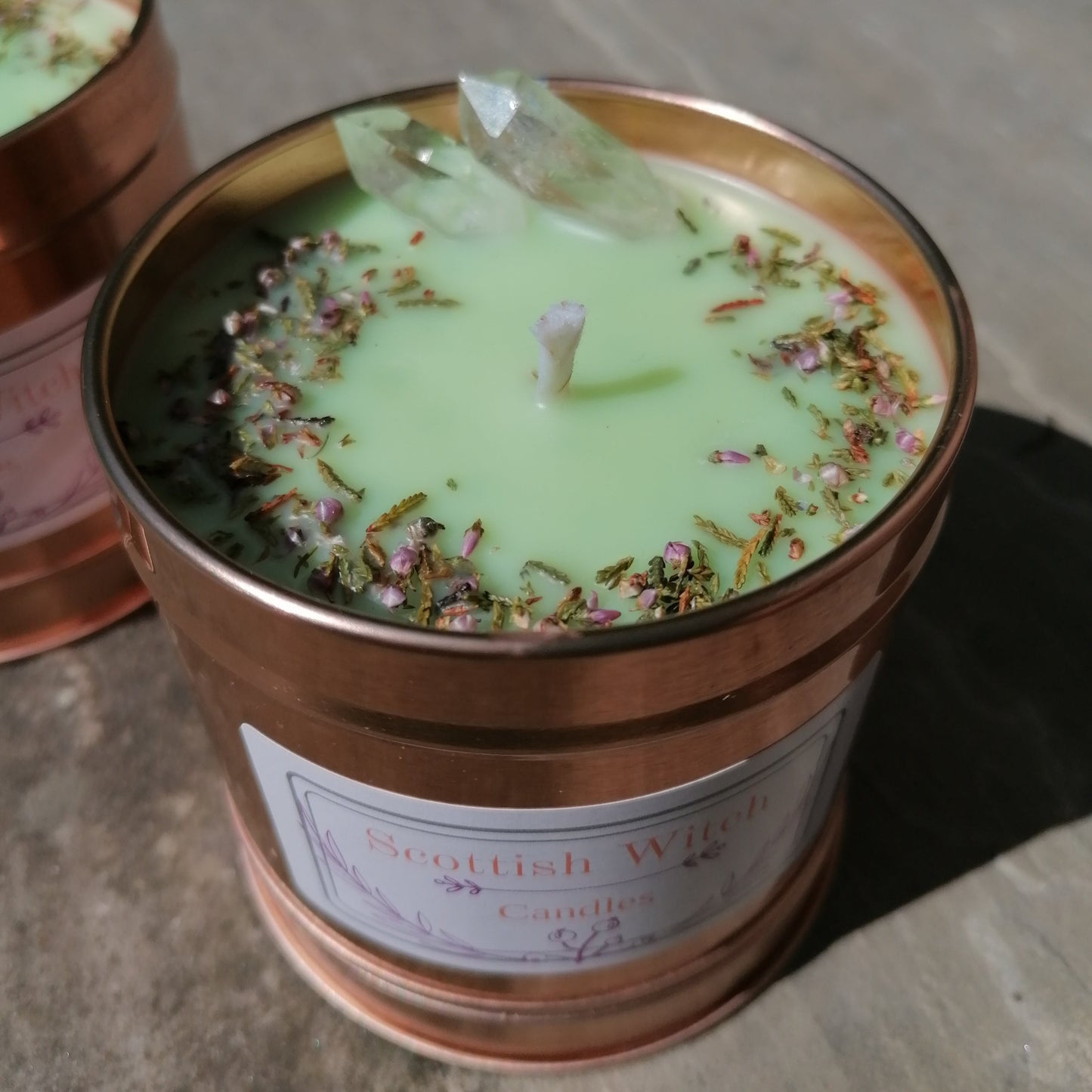 a green candle in a rose gold tin decorated with clear quartz crystals and scottish heather