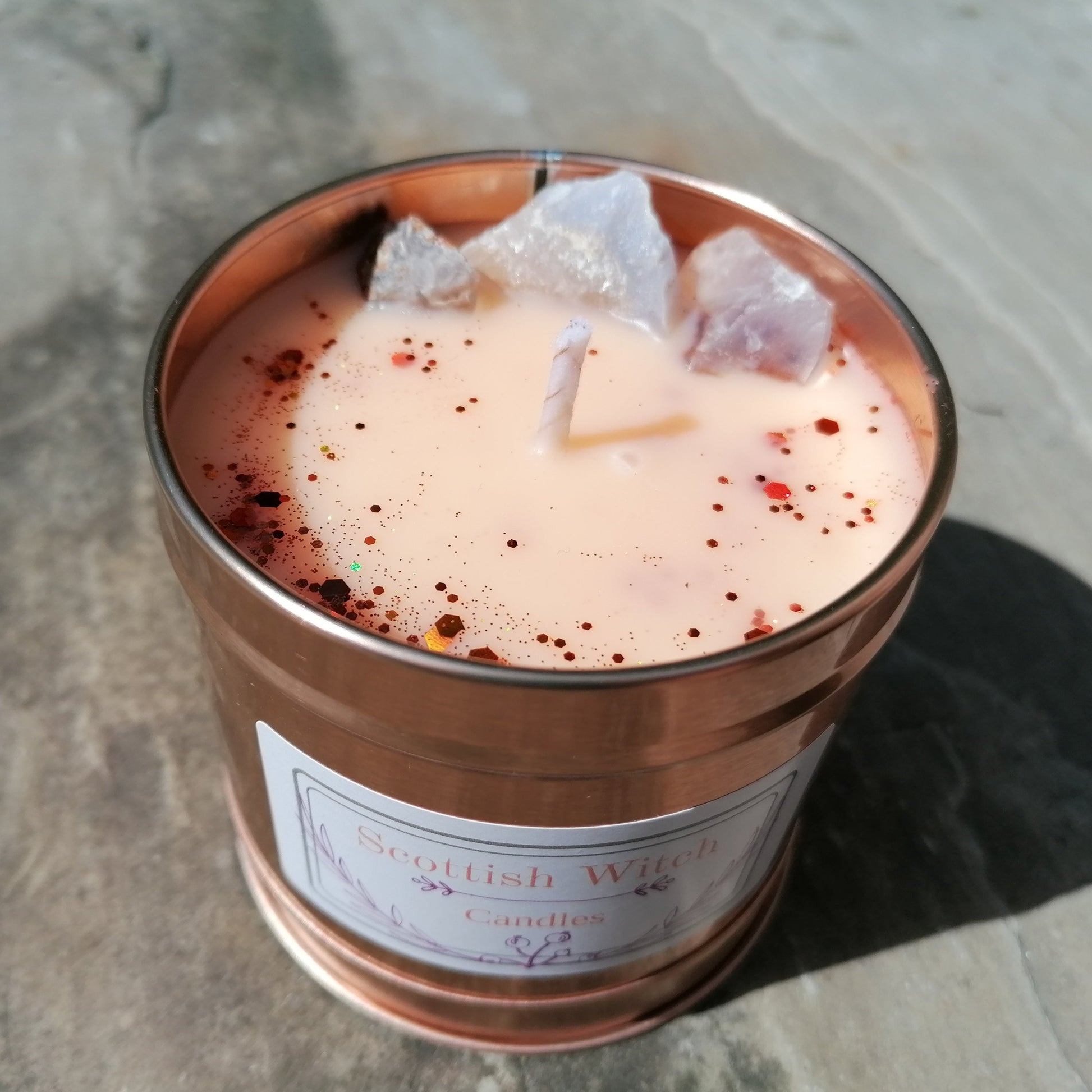 orange candle in a rose gold tin decorated with glitter and blue lace agate crystals