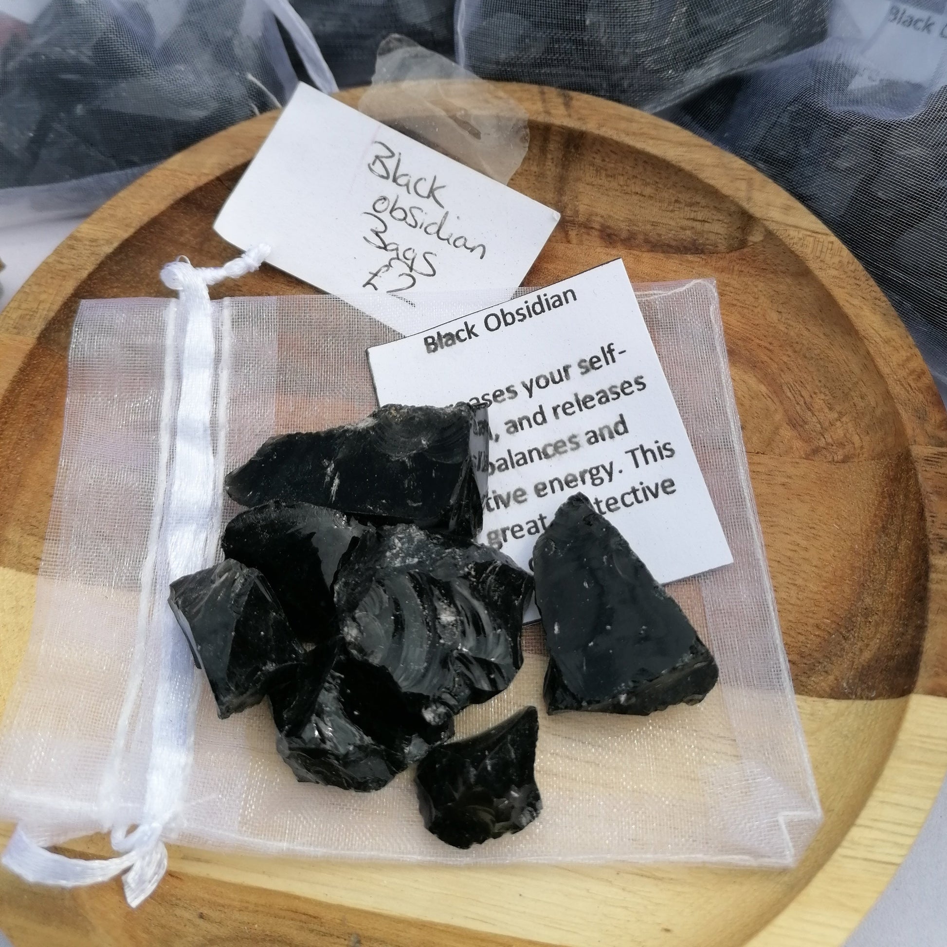 a handful of raw black obsidian chunks sitting on top of a small white organza bag