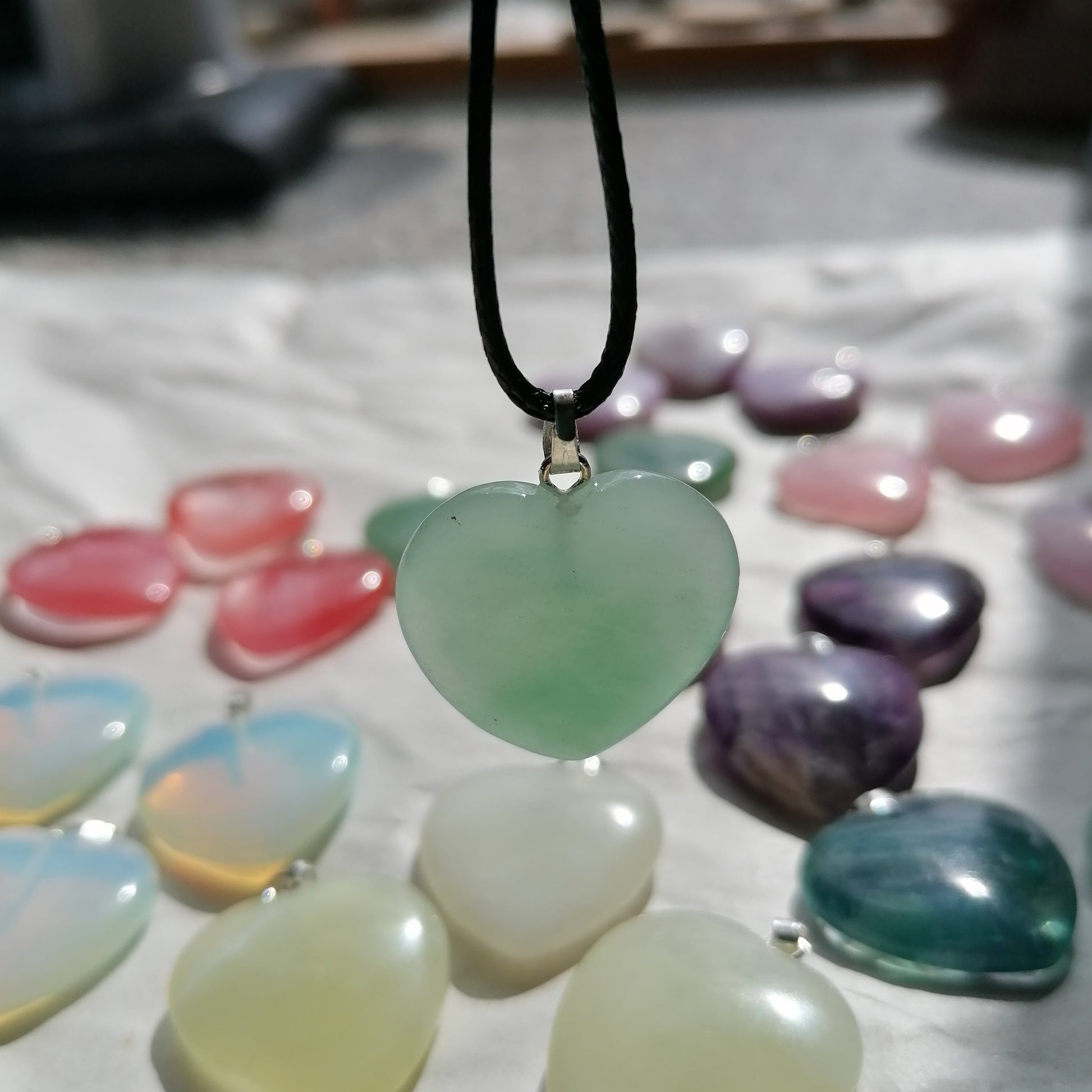 a green aventurine heart shaped crystal necklace on a black chord chain