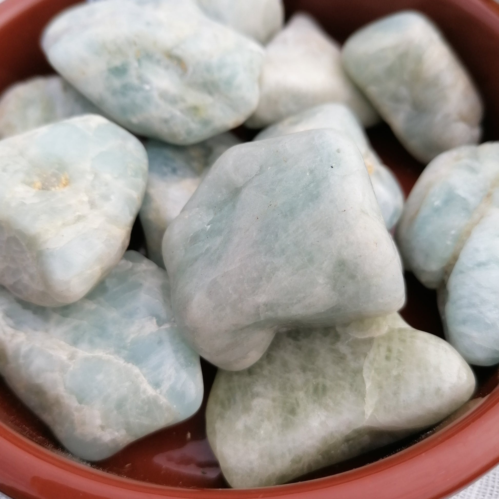 A brown dish of light green aquamarine crystal tumblestones