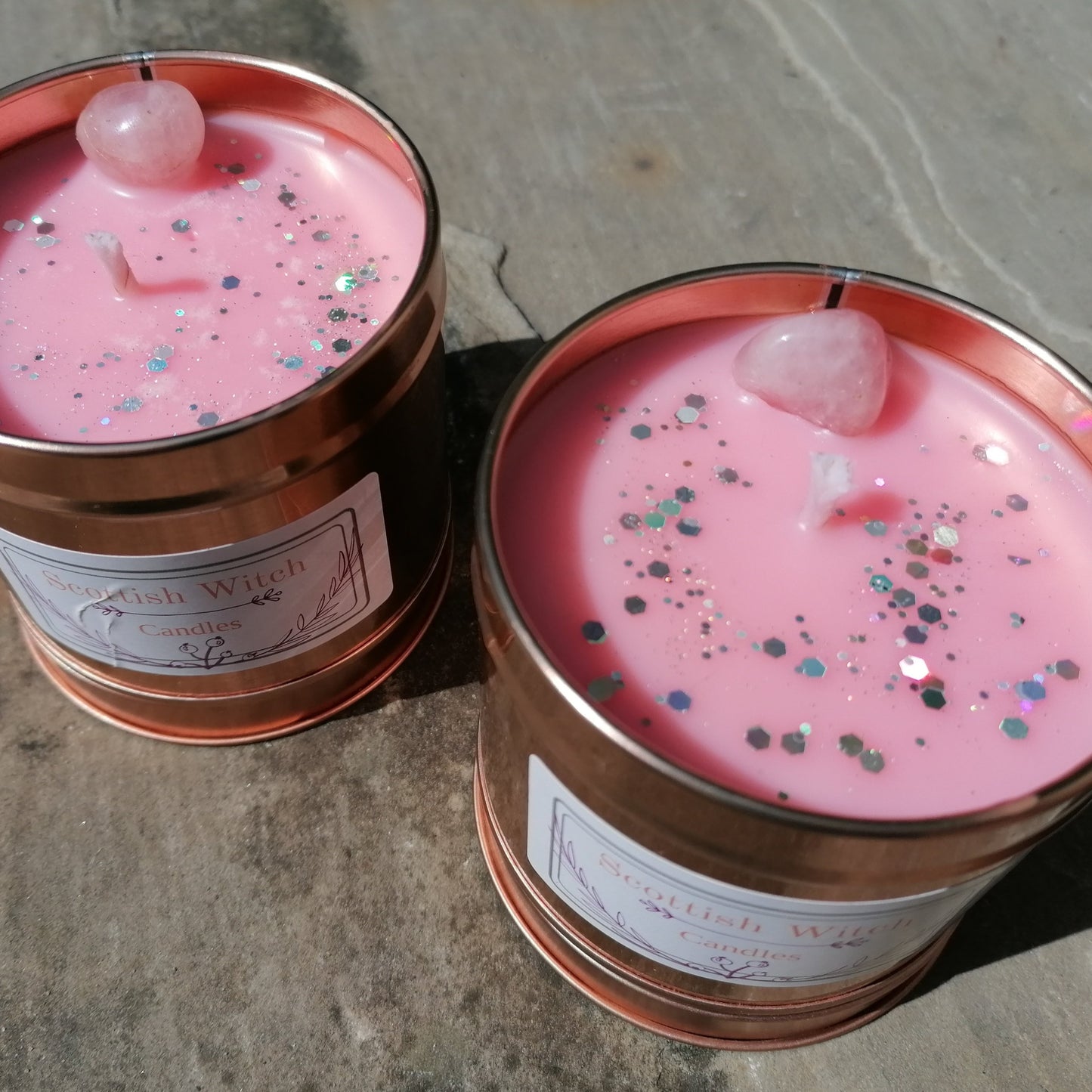 two pink candles in a rose gold tin decorated with silver glitter and a rose quartz crystal