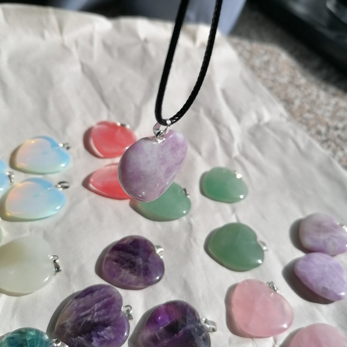 a purple and white Lepidolite heart shaped crystal necklace on a black chord chain