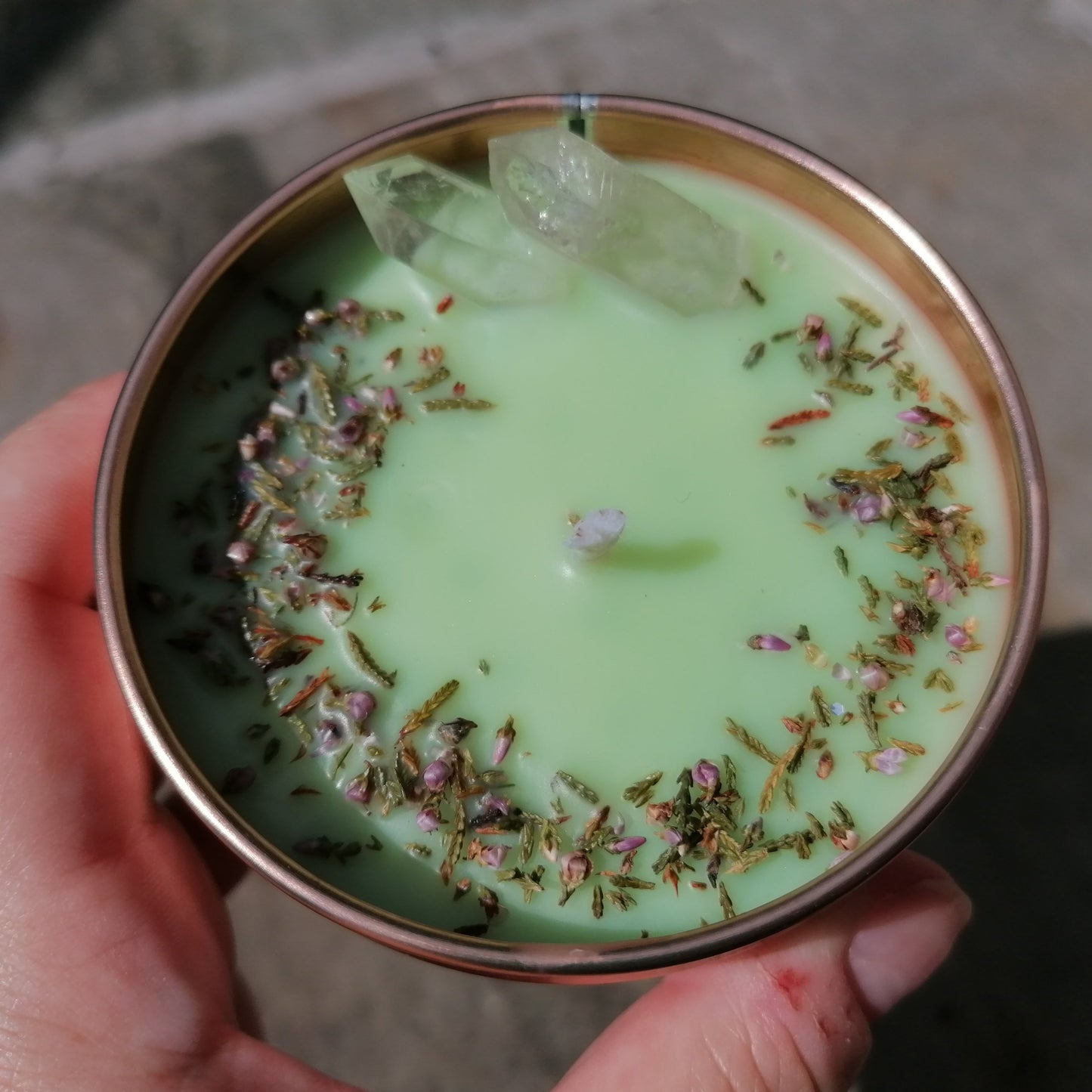 a green candle in a rose gold tin decorated with clear quartz crystals and scottish heather