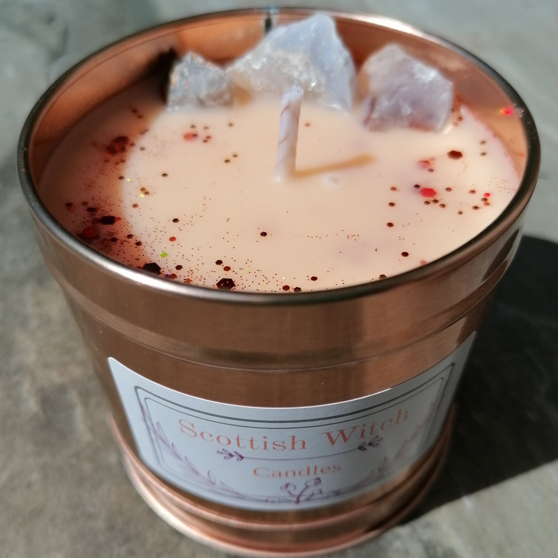 orange candle in a rose gold tin decorated with glitter and blue lace agate crystals