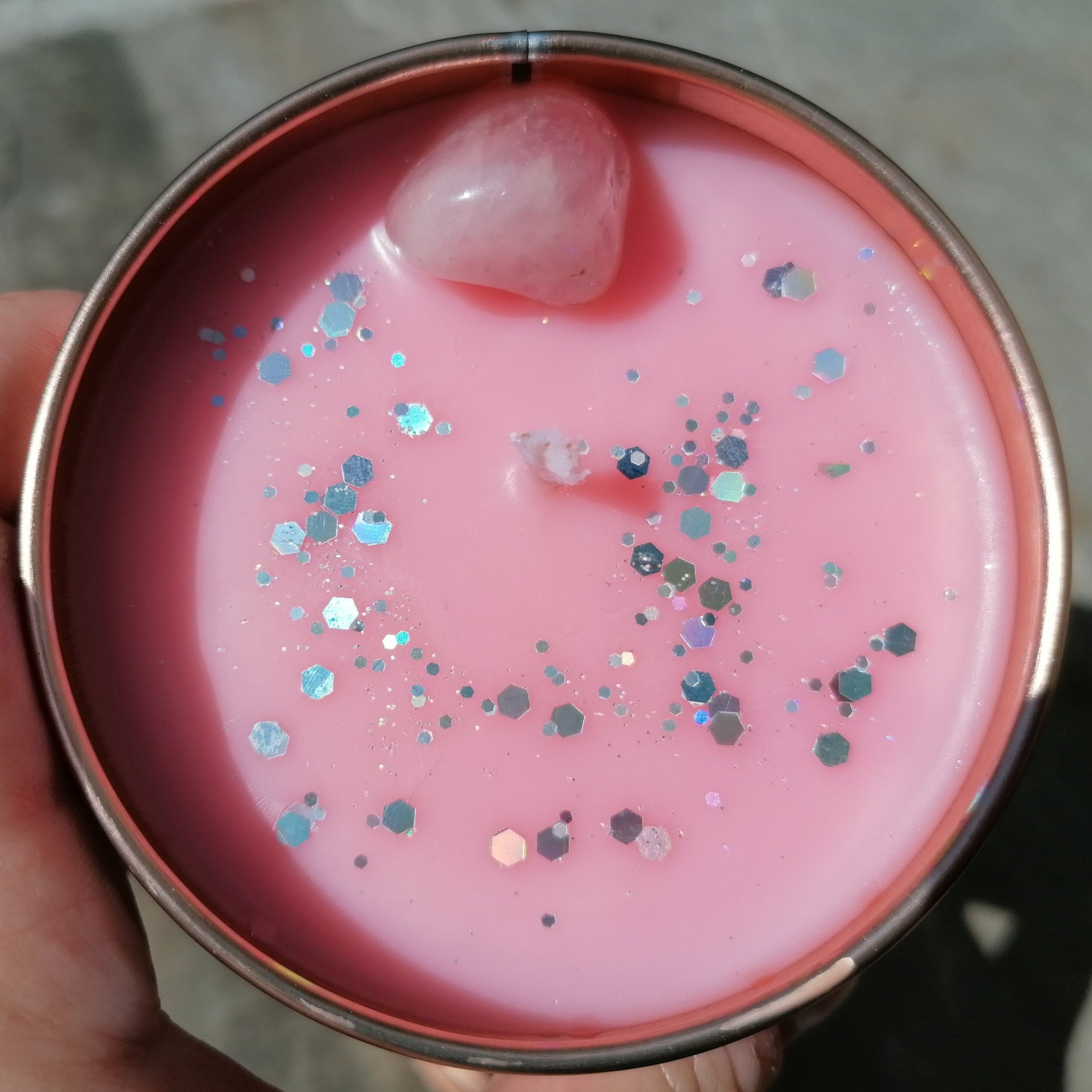 a pink candle in a rose gold tin decorated with silver glitter and a rose quartz crystal