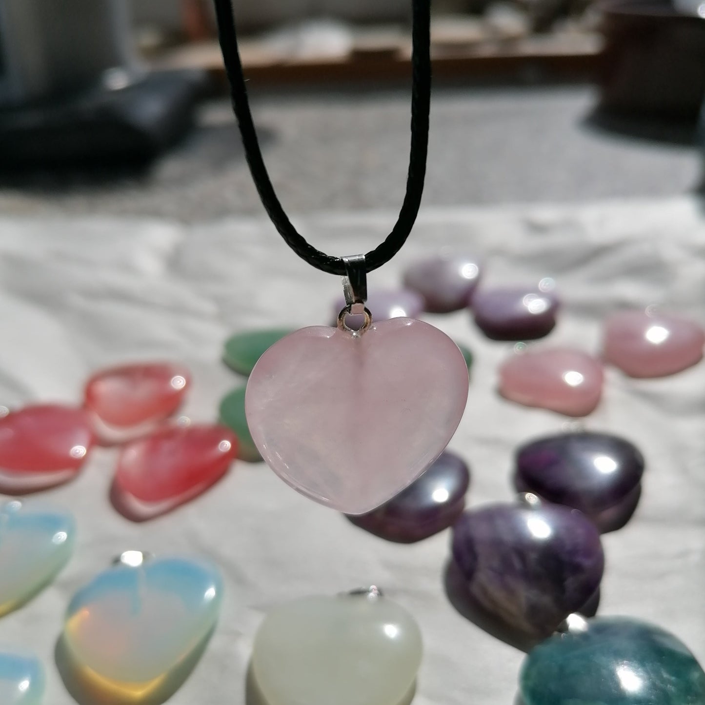 a pink rose quartz heart shaped crystal necklace on a black chord chain