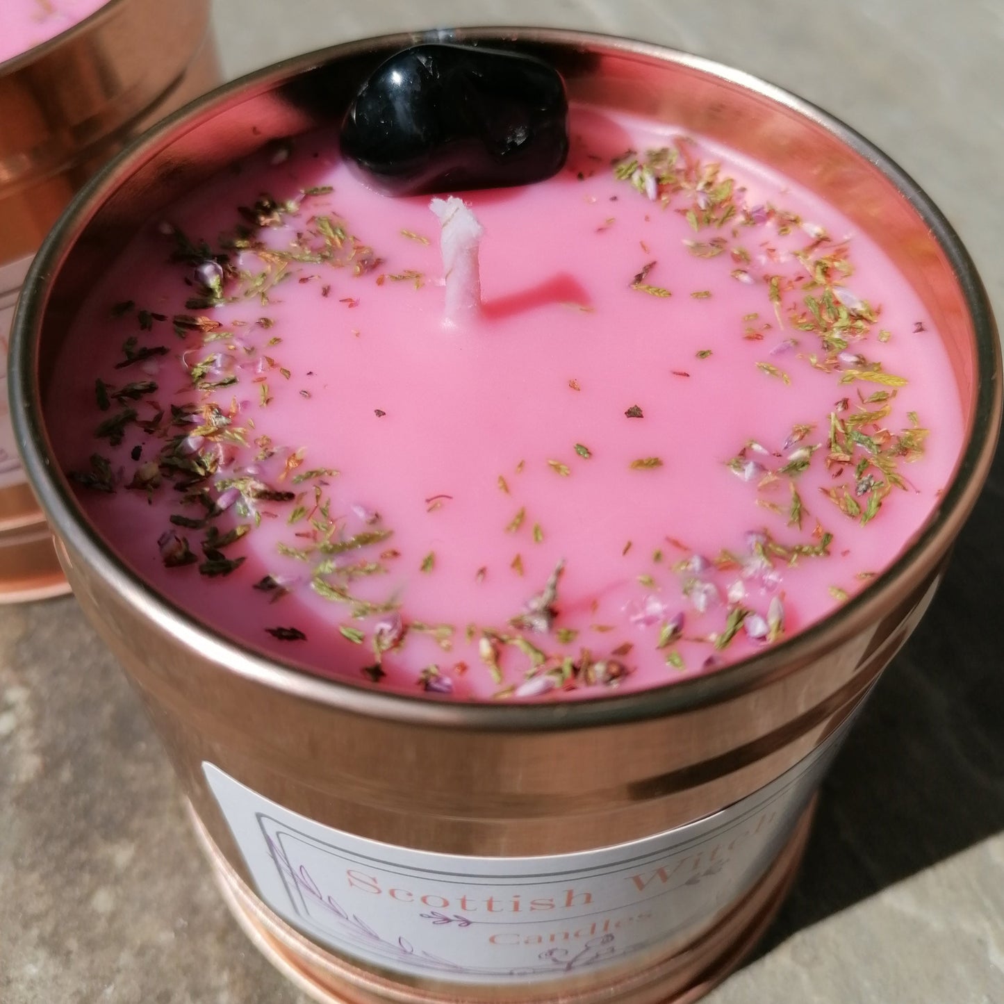 a pink candle in a rose gold tin decorated with a black onyx crystal and scottish heather