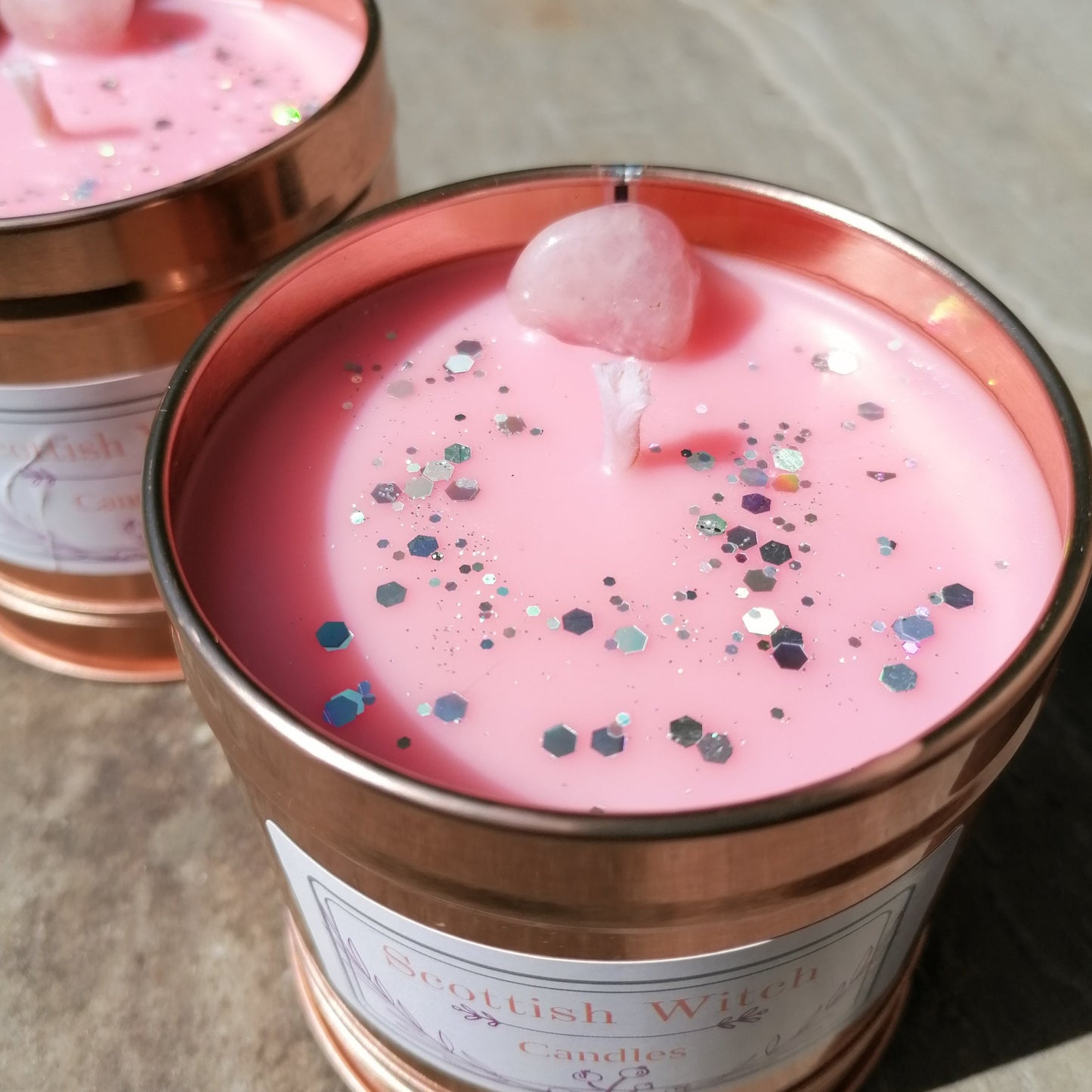 a pink candle in a rose gold tin decorated with silver glitter and a rose quartz crystal