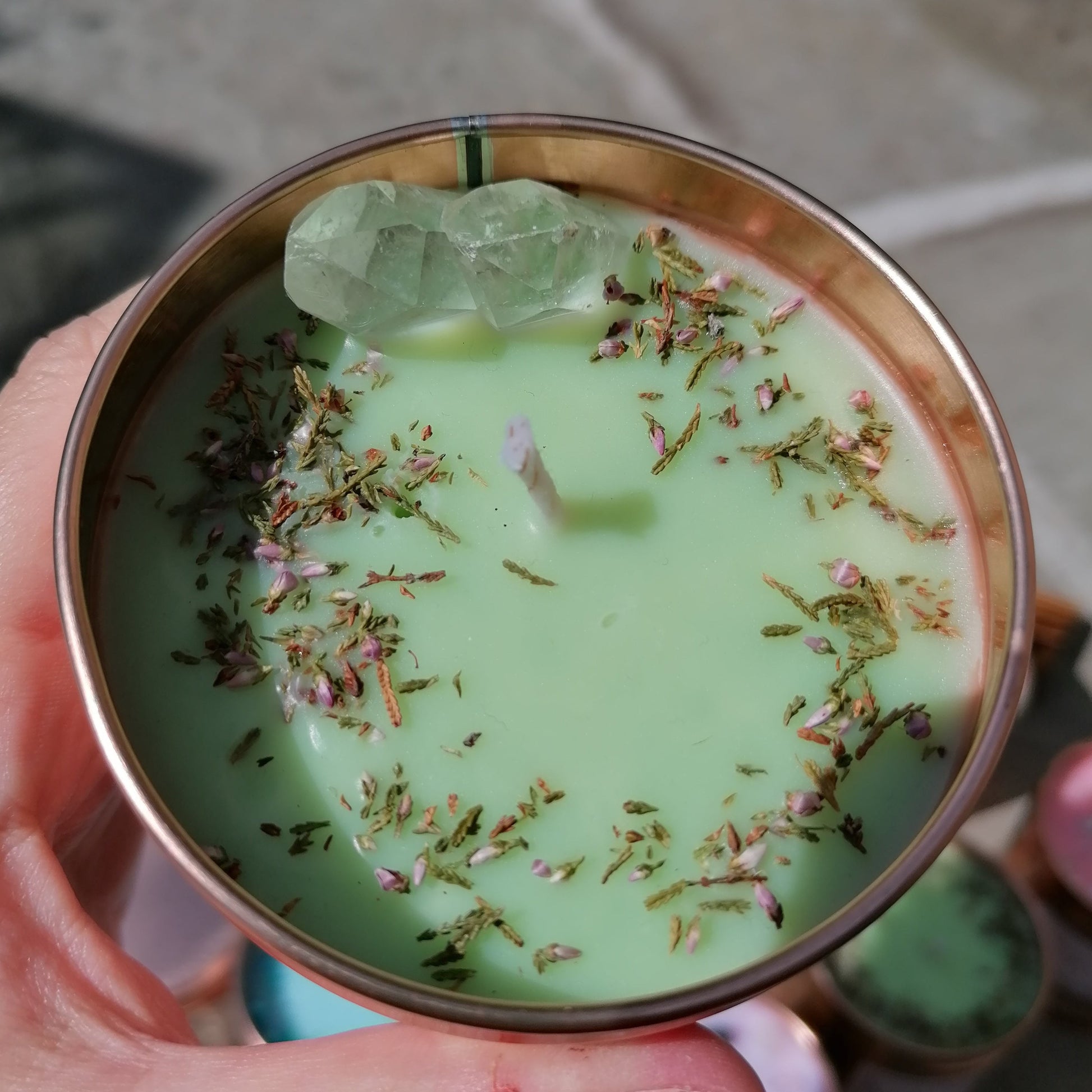 a green candle in a rose gold tin decorated with clear quartz crystals and scottish heather