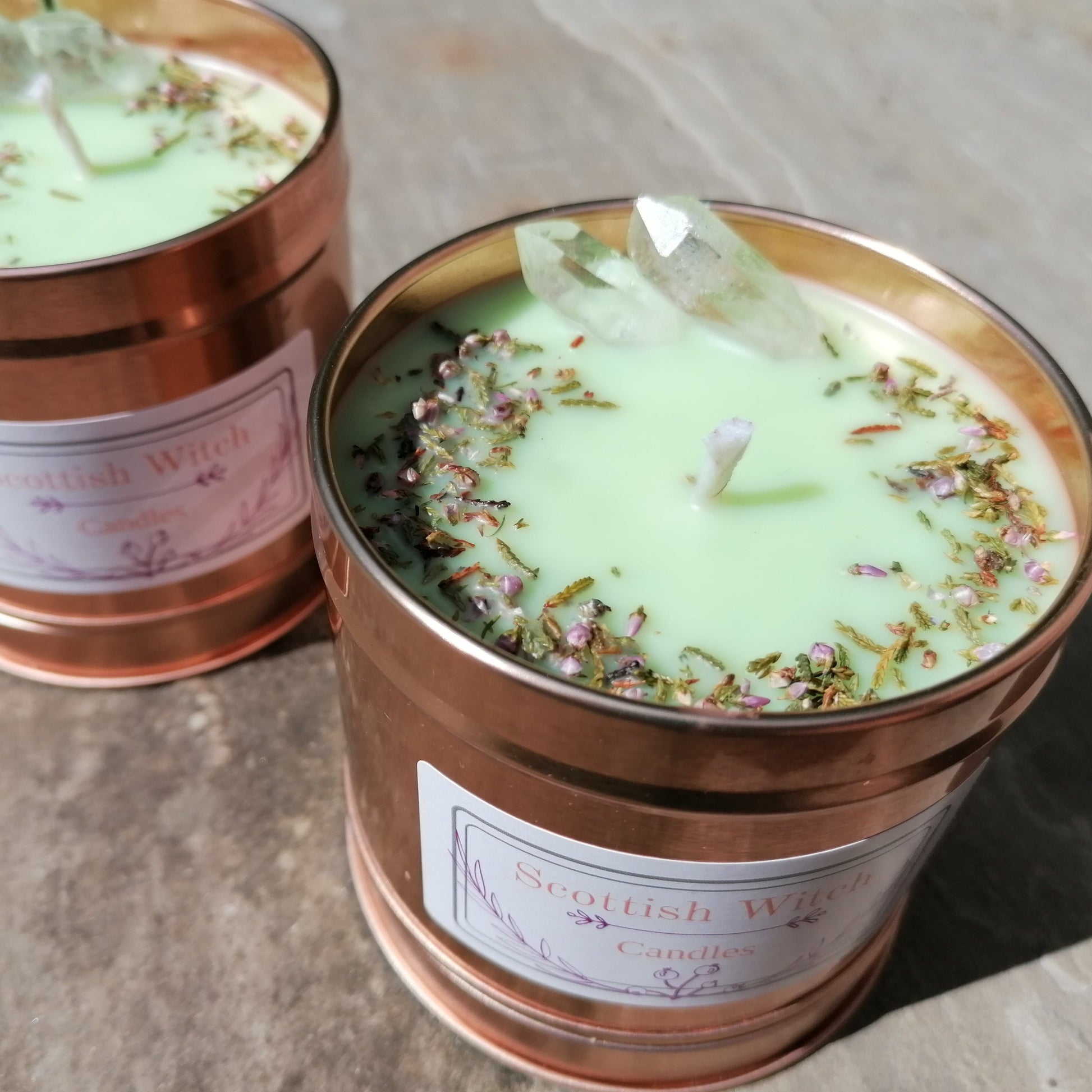 a green candle in a rose gold tin decorated with clear quartz crystals and scottish heather